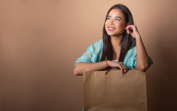 亚洲美女拿着纸质购物袋，展示环保可持续的包装，在孤立的背景上幸福地微笑，复制空间。图片下载