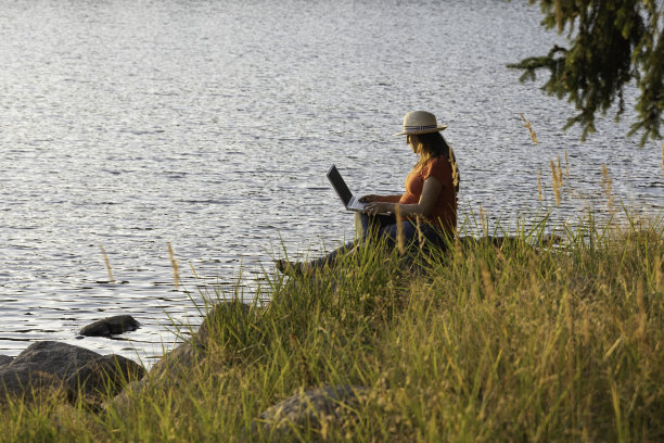 人与自然。怀孕的自由职业者在湖边用笔记本电脑工作。图片下载