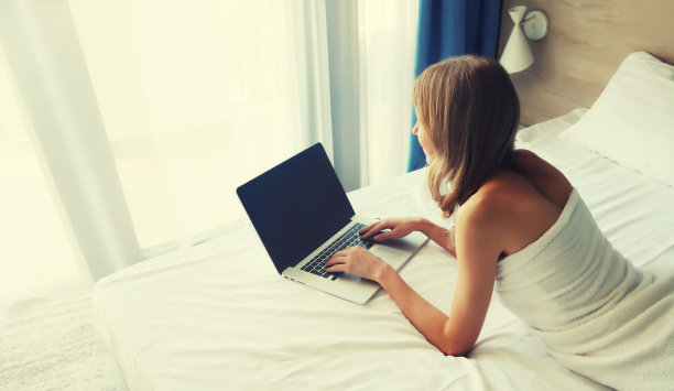 年轻女子躺在床上用笔记本电脑工作的照片图片下载