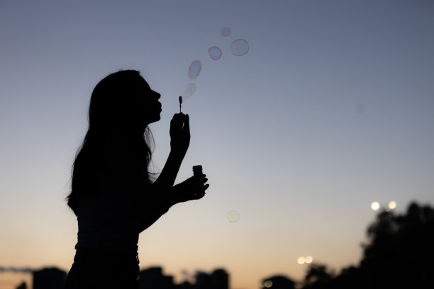 年轻女子玩泡泡棒的剪影。图片下载