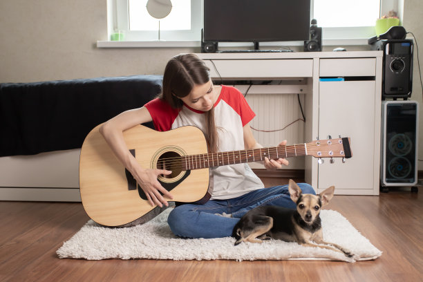 十几岁的女孩在家里的青少年房间里弹吉他，青少年音乐家在她的卧室里，一只小狗躺在旁边图片下载