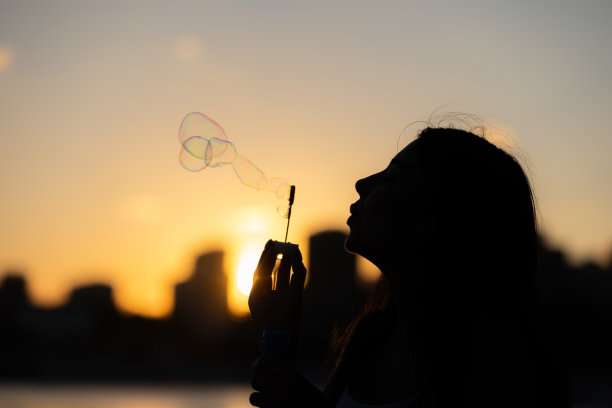 年轻女子玩泡泡棒的剪影。图片下载