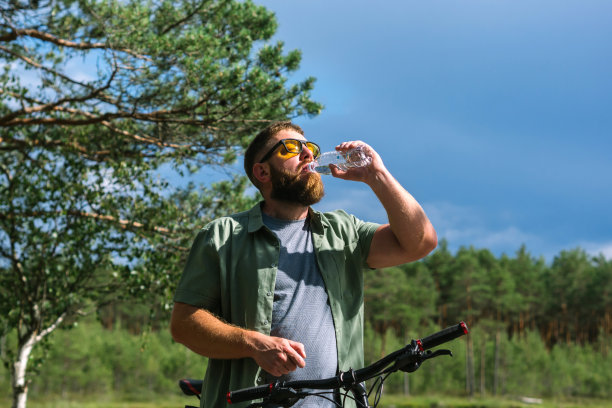 骑自行车的人可以在自行车附近休息，在森林里休息，在冒险锻炼中放松能量，喝一瓶水补水，在森林里享受健康。骑自行车的大胡子男子图片下载