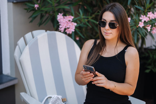 年轻女子在喝咖啡休息时使用手机的照片。一位女士坐在户外的椅子上图片下载