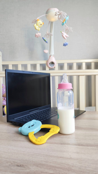 笔记本电脑，奶瓶，桌上的摇铃。工作休产假，带娃生活和工作休产假。带孩子的工作场所的组织图片下载
