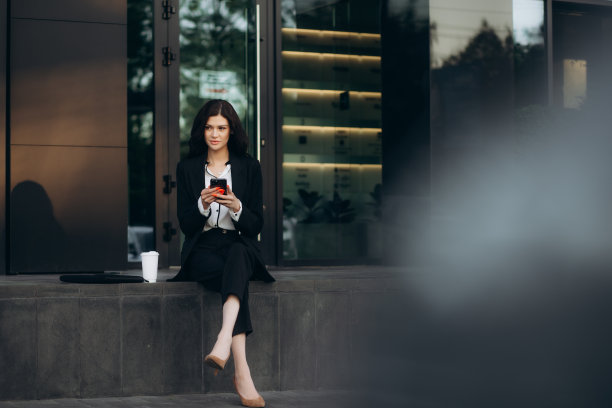 白人女商人走在街上，用智能手机和喝咖啡杯。喝咖啡休息时，美女在办公楼附近打字图片下载