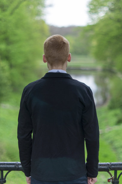 一个穿着夹克、红头发的年轻人站在桥上望着远方图片下载