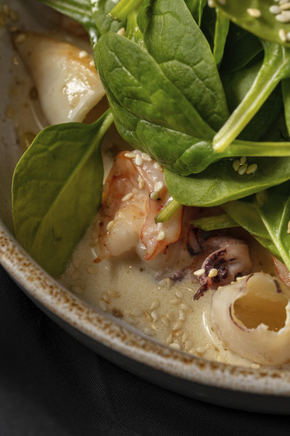 用白葡萄酒和奶油炖虾、鱿鱼和小章鱼的热沙拉，上面放上生菜。食物放在一个侧面高的轻质陶瓷盘子里。浅色背景上的陶器。图片下载