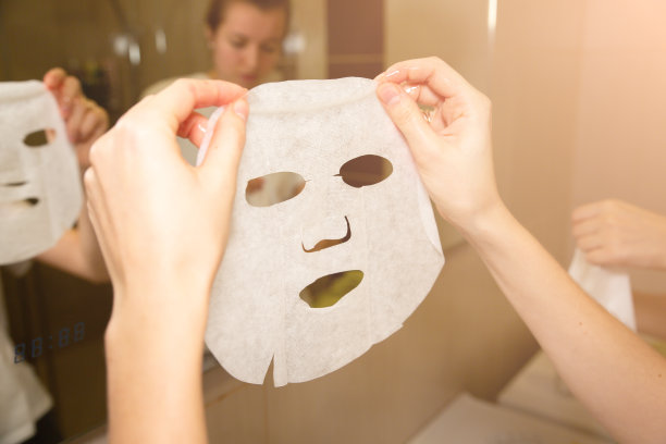 女孩手里拿着面膜片。在家做美容面部手术。图片下载