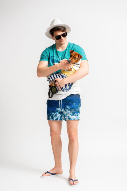 一个穿着沙滩装和人字拖的男人，怀里抱着一只杰克罗素梗犬图片下载
