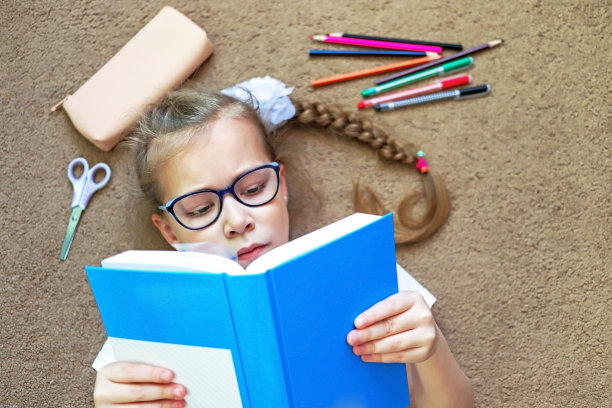 一个女孩坐在地板上看书，当她坐在书桌或桌子旁累了图片下载