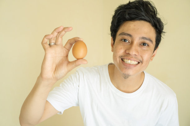 年轻人印尼握着鸡蛋微笑着，表情沉思。图片下载