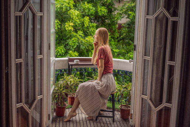 一个姜黄色头发的女人站在传统风格的阳台上享受她的早晨咖啡。欧洲或亚洲酒店里的一名妇女，旅游业正从大流行中复苏。由于接种疫苗，旅游业已经恢复。该女子在酒店被隔离了14天。图片下载