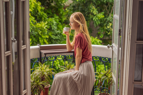 一个姜黄色头发的女人站在传统风格的阳台上享受她的早晨咖啡。欧洲或亚洲酒店里的一名妇女，旅游业正从大流行中复苏。由于接种疫苗，旅游业已经恢复。该女子在酒店被隔离了14天。图片下载