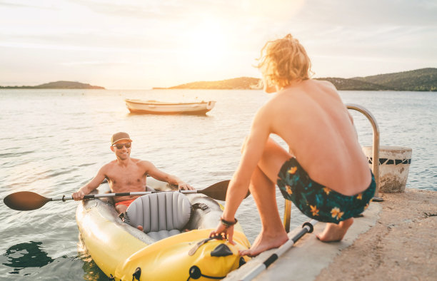父亲带着十几岁的儿子乘坐亮黄色的充气皮艇，傍晚从克罗地亚的亚得里亚海海港附近的西贝尼克市返回。度假和家庭价值观垂直的形象。图片下载