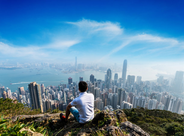 年轻人坐在山顶上，看着香港的天际线图片下载