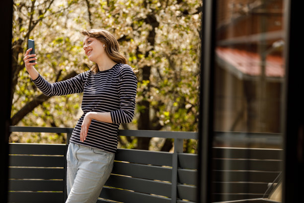 年轻女子在阳台上放松，和朋友视频聊天图片下载