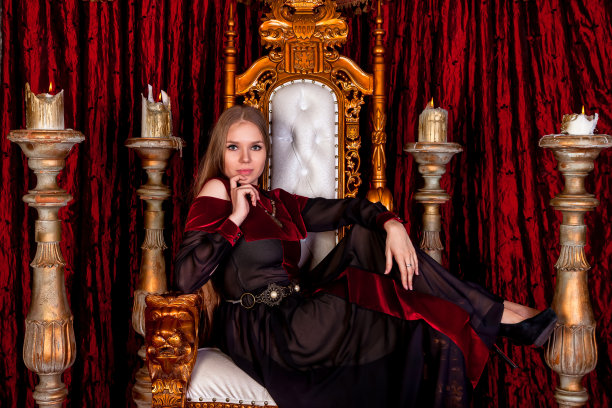 可爱的历史形象的女士坐在古色古香的王座堡垒，看着镜头。中世纪女王在城堡房间的金色宝座上摆姿势。剧场表演的概念。复制文本空间图片下载