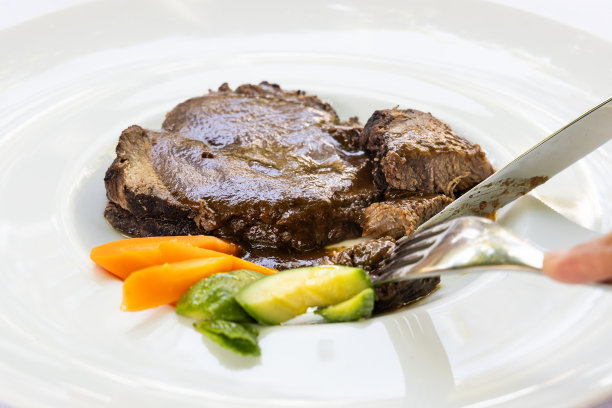 用刀叉切割白色大盘子上的意大利牛排的特写图片下载
