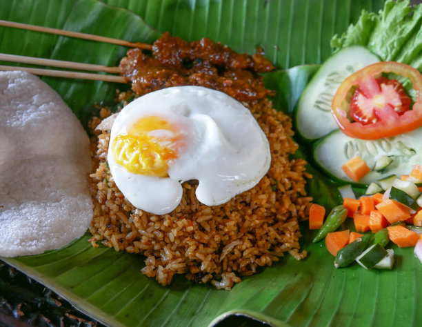 炒饭或炒饭，有沙茶或鸡肉沙茶和花生酱或bumbu kacang，一个单面煎蛋，番茄沙拉，黄瓜和生菜，虾饼干。腌菜或辣椒和香蕉叶一起上桌。图片下载