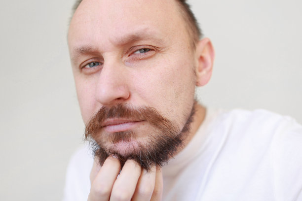 剪短的镜头男人的手是无限制的抓挠未剃光的下巴。一个穿着白色t恤，留着浓密胡须的粗壮男人。美容院概念，理发店图片下载