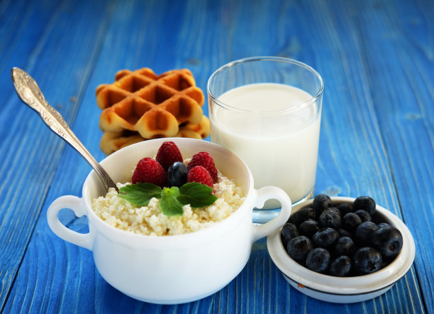 蓝木桌上放着一杯牛奶，碗里装着白干酪和浆果。图片下载