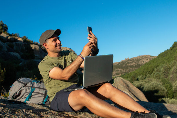 戴帽子的男人带着笔记本电脑和手机去山上工作图片下载