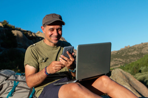戴帽子的男人带着笔记本电脑和手机去山上工作图片下载