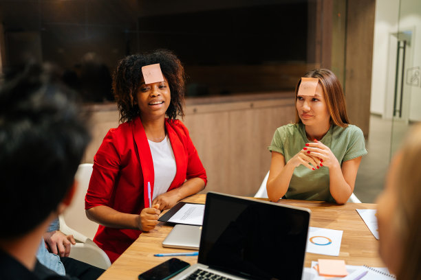 形形色色的快乐商业团队下班后在额头上贴便利贴玩猜谜游戏。一群快乐的同事玩得很开心图片下载