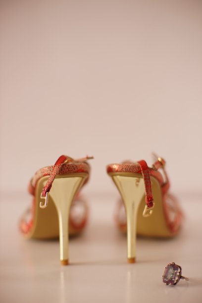 金色细跟的红色夏日凉鞋，白色的桌子上点缀着神秘的黄玉戒指。图片下载