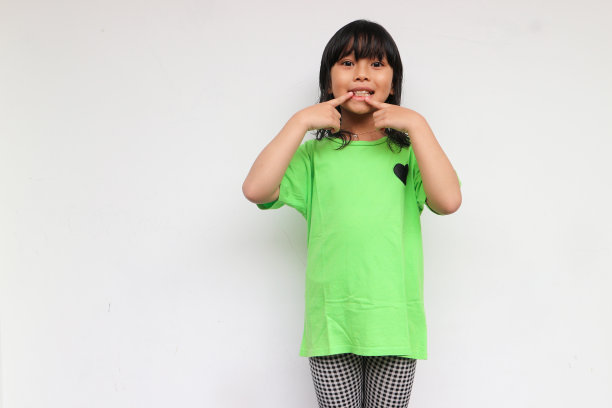 一个笑着的小女孩举起手来指着她的牙齿图片下载