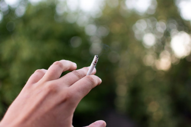 在大自然的背景下，手抽着闷烧的香烟。图片下载