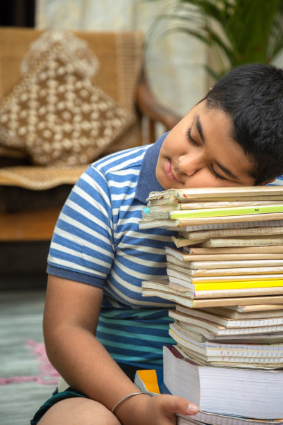 压力大的印度学生男孩睡在一堆书上图片下载