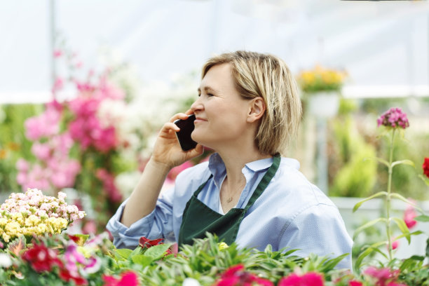小企业主，快乐的女人坐在花店的鲜花旁服务工作。白人女孩成功的主人环境肖像，侧面图片下载