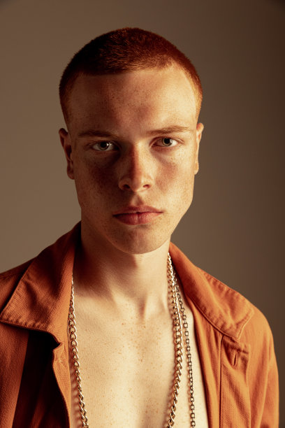 特写肖像英俊的红头发的年轻人与雀斑的脸摆，聚精会神地看着相机孤立在棕色的工作室背景图片下载