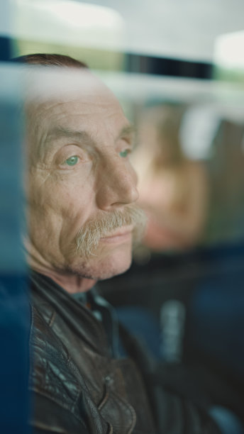 在火车车厢里旅行时，沉思的老人看着窗外，透过玻璃观看图片下载