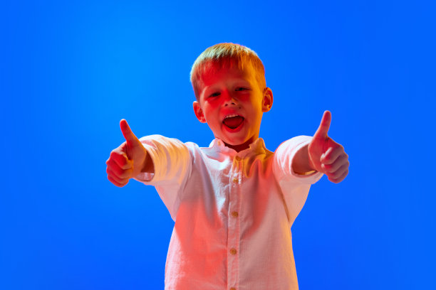 肖像积极的小男孩在白色衬衫设计与微笑对蓝色工作室背景霓虹灯图片下载