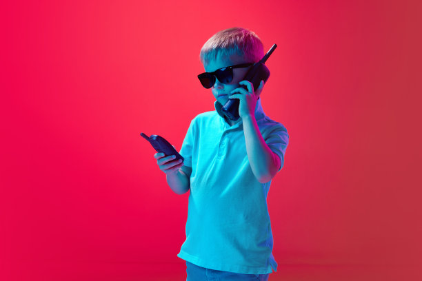 小男孩，孩子说话的复古，旧手机在霓虹灯粉红色工作室背景。认真的看图片下载