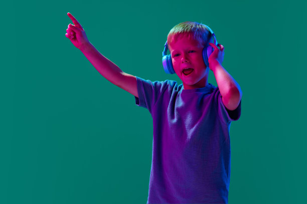 享受。孩子，小男孩在霓虹灯下戴着耳机听音乐图片下载