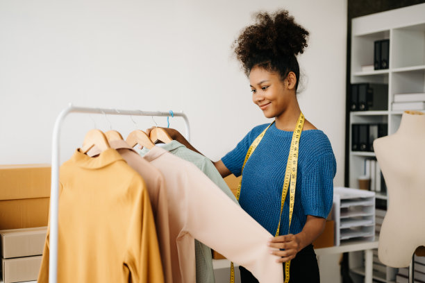 在时尚设计师的现代办公室里，冷静的卷发黑发女人坐在桌子上，手里拿着平板电脑和智能手机。图片下载