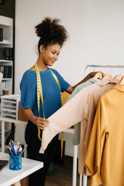 在时尚设计师的现代办公室里，冷静的卷发黑发女人坐在桌子上，手里拿着平板电脑和智能手机。图片下载