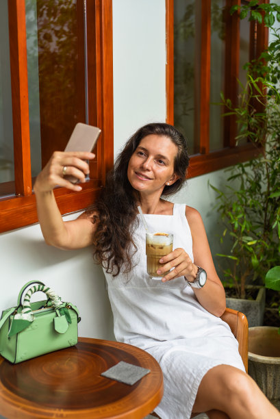 40岁的俄罗斯女人素颜，穿着白裙子，端着一杯冰咖啡坐在那里自拍图片下载