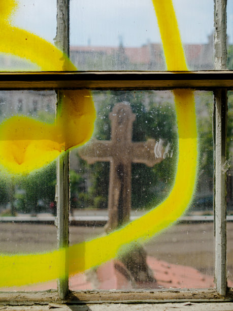 废弃建筑的旧窗户上的黄色涂鸦和窗户后面的石头十字架图片下载