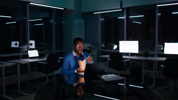 非裔美国商人在黑暗的办公室工作到很晚，吃外卖图片下载