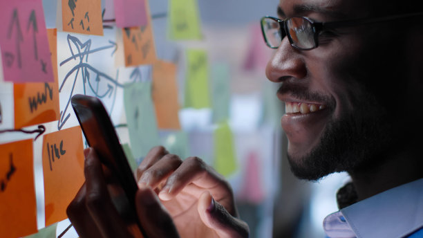 近距离的微笑的非洲裔美国商人看玻璃板上的笔记和使用智能手机图片下载