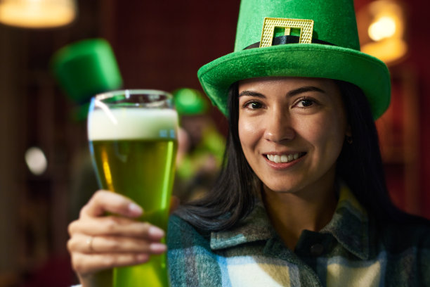 把注意力集中在拿着一杯绿啤酒微笑着的黑发女人身上图片下载