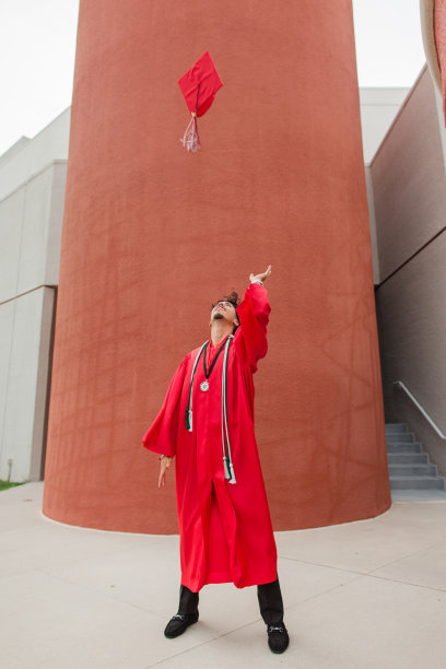 2023年高中毕业生，18岁的棕色头发和棕色眼睛的年轻人，穿着红色毕业礼服，高中毕业后高兴地把他的红色帽子和流苏扔在他头顶的空中图片下载