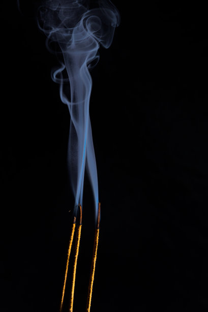 三个金色的香燃烧和蓝色的烟上升到顶部的特写图像。副本的空间。图片下载