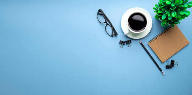 平铺，俯视图办公桌书桌。工作空间，笔记本电脑，办公用品，铅笔，绿叶，和咖啡杯的蓝色背景。图片下载