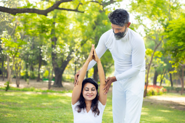 印度男老师或教练在公园里教年轻的女学生瑜伽，两人一起在户外做伸展健身运动，运动和锻炼的概念。图片下载